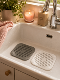 Grey and white silicone drain blockers sitting in a white kitchen sink