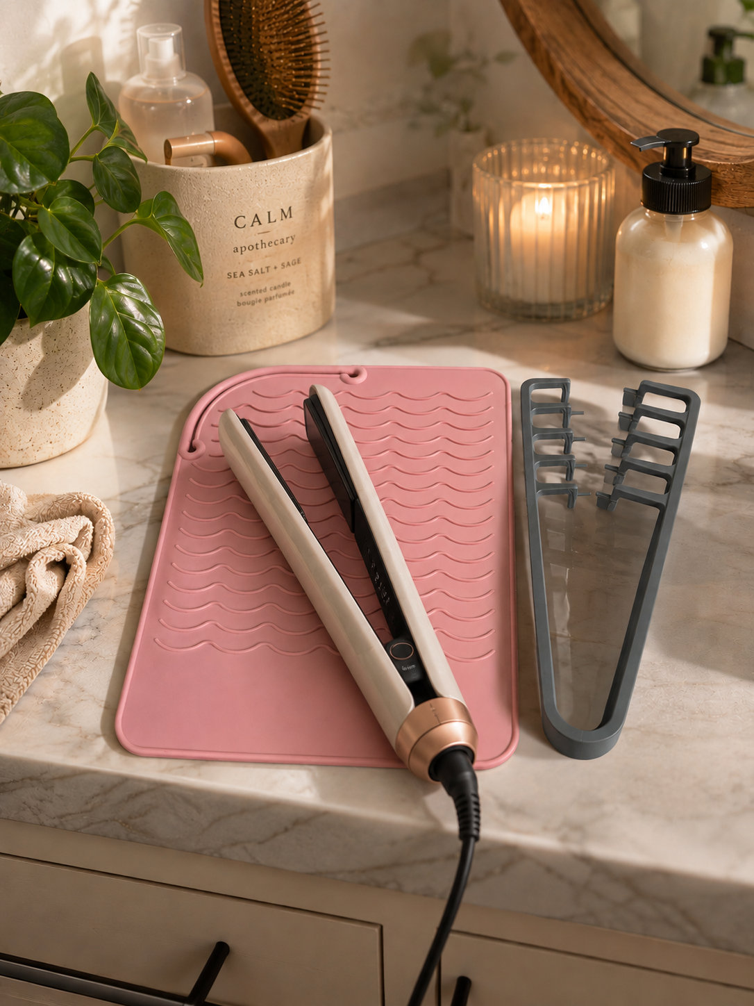 Hair straightener resting on pink heat resistant mat with grey holder alongside