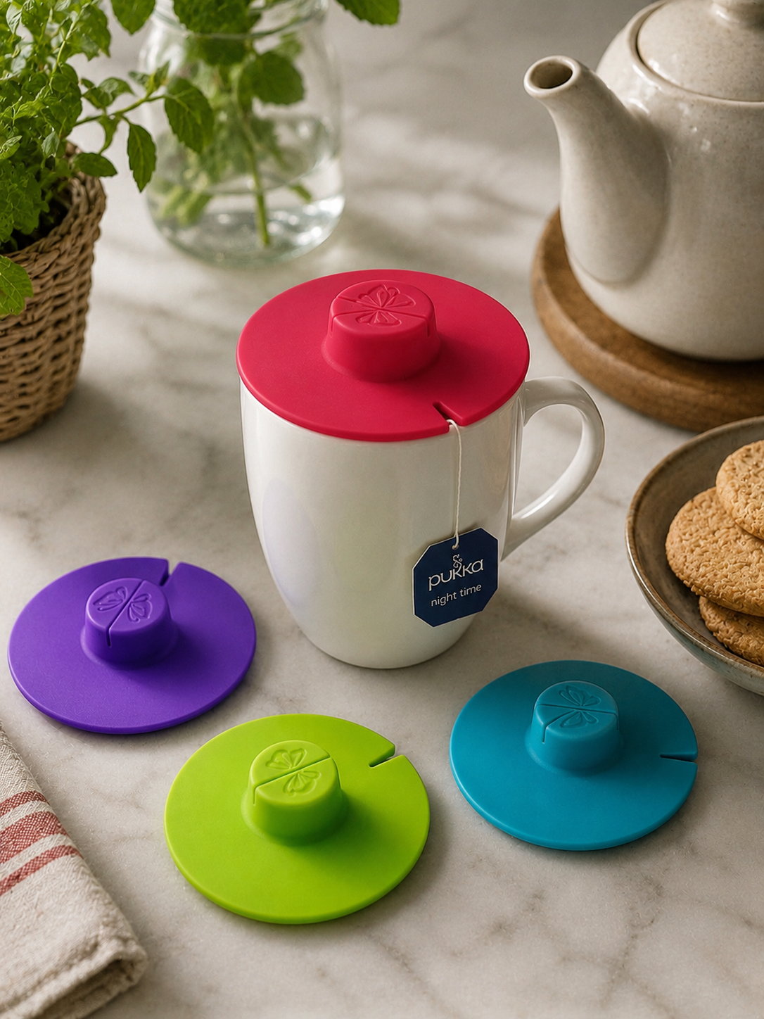 Silicone mug lid teabag covers in pink, purple, lime green and teal, shown with a white mug and Pukka teabag