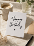 Minimalist Happy Birthday card with script typography and small heart, displayed on a marble surface with coffee and eucalyptus